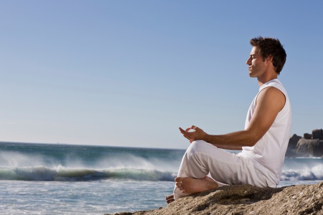 Young man meditating on rock by sea