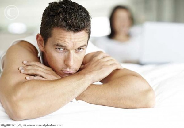 Bored man in bed with woman using laptop