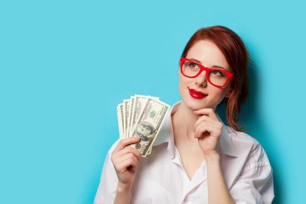 Portrait of redhead women in red glasses with money on blue background