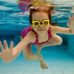 The girl smiles, swimming under water in the pool